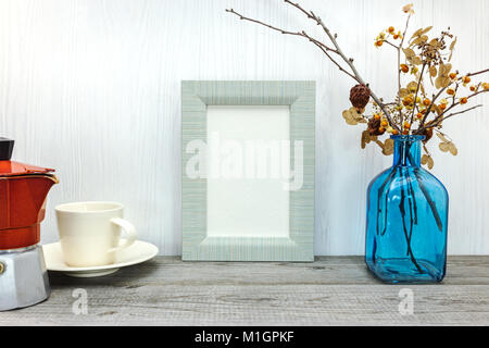 Cafetière, tasse vide, cadre photo et vase avec fleurs pressées sur planche en bois gris Banque D'Images