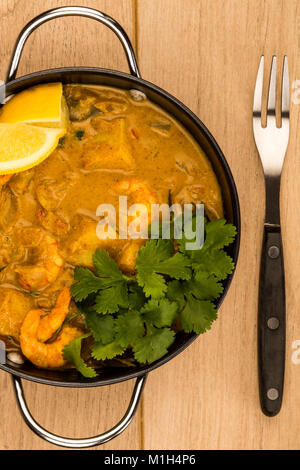 Sri Lanka King Style Gambas au curry avec du citron et de la coriandre herbes sur une table en bois clair Banque D'Images