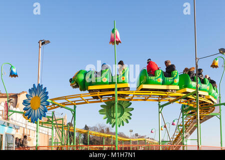 Les parents et les jeunes enfants sur un Roller Coaster ver loufoque à un Saisonnier hiver fête foraine du Castello, Venise, Italie montrant la voie against a blue sk Banque D'Images