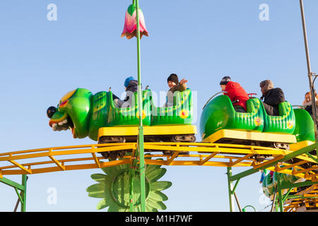 Les enfants et les parents à cheval sur un Roller Coaster ver loufoque à une fête foraine ou amusement park contre un ciel bleu ensoleillé dans un close up side view Banque D'Images