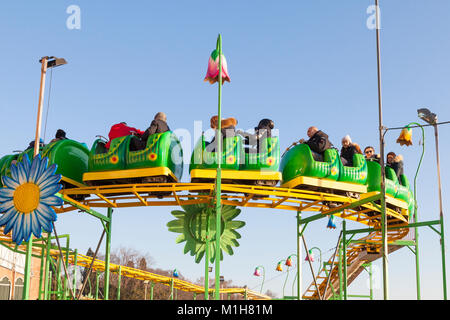 Groupe de jeunes enfants avec leurs parents à cheval sur un roller coaster Wacky Worm à Venise, Italie contre un ciel bleu montrant la voie lors d'un w de saison Banque D'Images