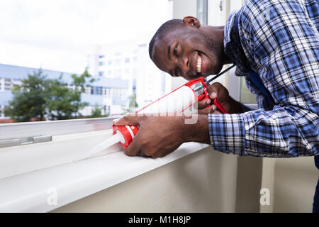 Close-up d'un jeune travailleur homme d'appliquer un joint en silicone avec des armes à feu en silicone Banque D'Images