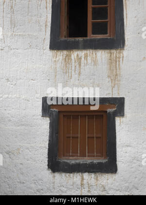 Deux fenêtres en bois vintage sur un mur blanc d'une maison tibétaine, traditionnellement les fenêtres sont entourées de peinture noire, la protection contre le mal. Banque D'Images