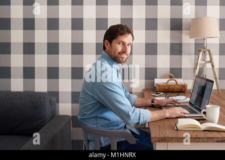 Heureux bel homme travaillant à la maison sur un ordinateur portable Banque D'Images