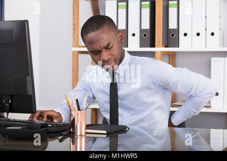 Les jeunes hommes et femmes souffrant de maux de dos en travaillant sur Computer in Office Banque D'Images