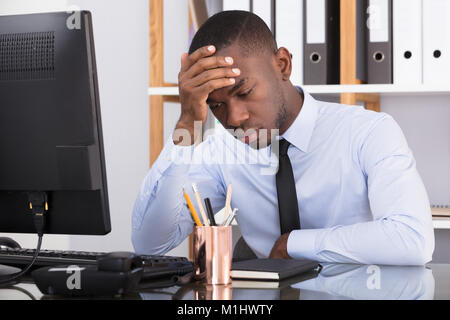 Homme a souligné avec la tête dans la main At Desk In Office Banque D'Images