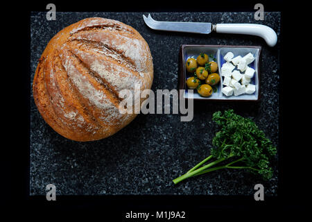 Sur pain de grains entiers en marbre gris bleu avec des olives vertes, le fromage feta et le persil frais, sur dark navy table cloth Banque D'Images