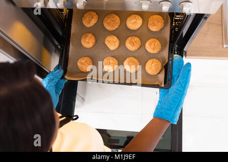 Main humaine portant des gants bleu en tenant le bac de petits gâteaux à partir de micro-ondes Banque D'Images