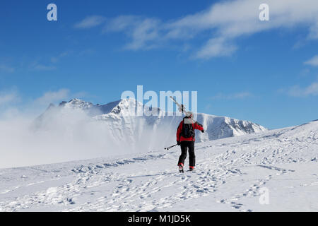 Avec skieur skis sur l'épaule aller jusqu'en haut de la montagne dans le froid soleil jour. Dans le brouillard d'hiver montagnes du Caucase, la Géorgie, la région Gudauri, Mt. Kudebi. Banque D'Images