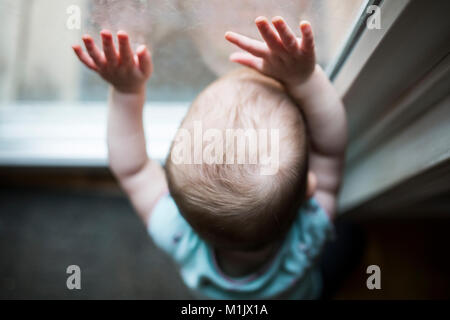 Portrait de bébé avec les mains sur la fenêtre Banque D'Images