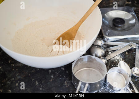 Cuvette de mélange contenant de la farine blanche à côté de tasses à mesurer et cuillères Banque D'Images