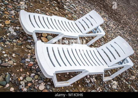 Deux chaises longues en plastique blanc sur une plage de galets de près. Banque D'Images