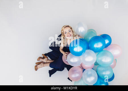 Femme blonde en robe bleu avec bleu et rose baloons regarde et sourit de l'appareil photo Banque D'Images