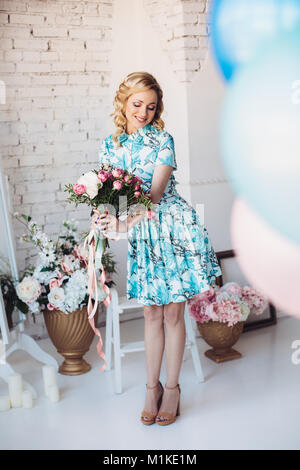 Femme blonde en robe bleu clair avec des fleurs en choisissant l'avant du mur de lumière Banque D'Images