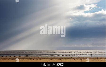 Un homme et femme marche un chien sur la plage à l'Est Brean côte du Somerset comme une douche lourde de pluie s'efface pour révéler le ciel bleu et le soleil Banque D'Images