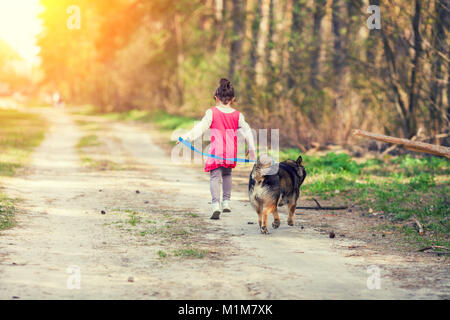 Heureuse petite fille jouant avec un chien piscine en été. Girl holding le chien en laisse et d'exécution sur chemin de terre le long de Forest Banque D'Images