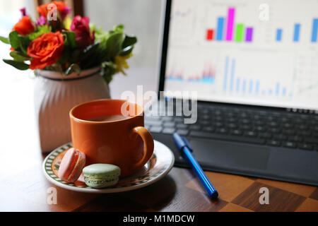 Tasse de café avec du lait sur la table sur un avant-plan à côté de l'ordinateur de travail et vase avec de belles fleurs bouquet sur une faible profondeur de champ Banque D'Images