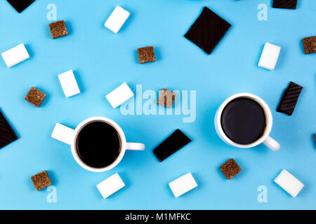 Deux tasses de café, les cubes de sucre brun et blanc et chocolat prieces sur fond bleu Banque D'Images