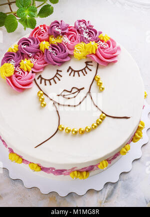 Gâteau de fête avec des fleurs crème et une fille visage sur un fond clair Banque D'Images