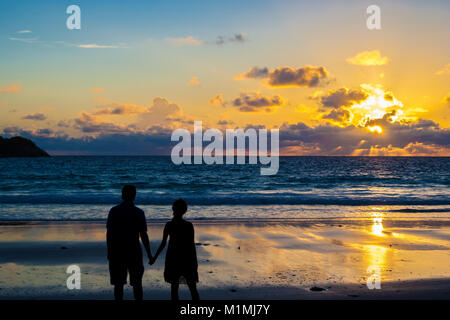 Vue arrière de la silhouette d'un couple d'amoureux se tenant la main pendant le coucher du soleil sur une plage. Banque D'Images
