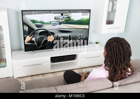 Girl Sitting on Couch jouer à des jeux de voiture de course à la maison Banque D'Images