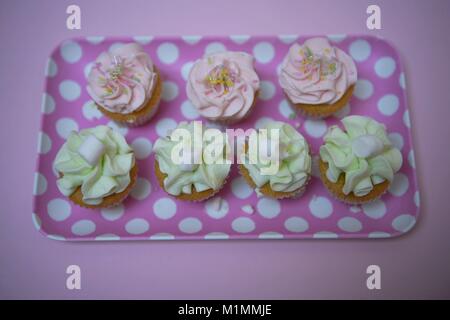 Belle mini cupcakes pastel de couleurs posées sur un petit plateau avec motif à pois sur fond rose Banque D'Images