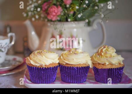 Délicieux cupcake à la crème de vanille sur une dentelle ancienne vintage table cloth et floral théière en arrière-plan avec des fleurs fraîches Banque D'Images