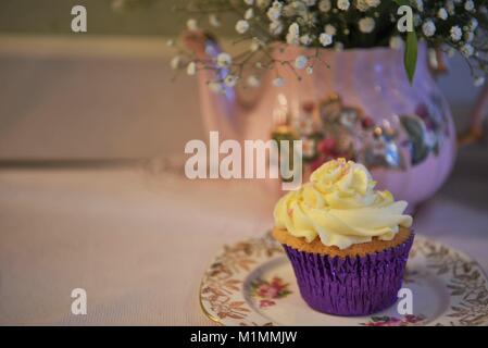 Délicieux cupcake à la crème de vanille sur une dentelle ancienne vintage table cloth et floral théière en arrière-plan avec des fleurs fraîches Banque D'Images