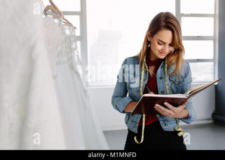 Designer de mode féminine travaillant dans robes de stocker et d'écrire dans un journal intime. Femme magasin nuptiale propriétaire dans sa boutique. Banque D'Images