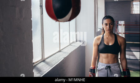 Boxer se tenant debout à l'intérieur d'un studio de boxe. Dans son boxer femme gants de boxe boxe près d'un sac de vitesse. Banque D'Images