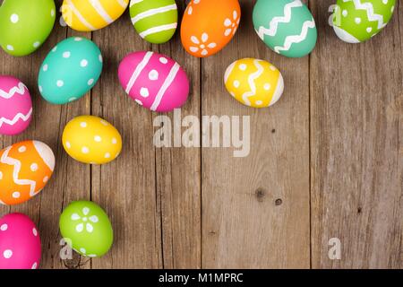 Oeufs de Pâques colorés frontière contre l'angle d'un fond de bois rustique Banque D'Images