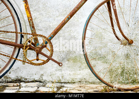 Détail détaillé d'un vélo abandonné rouillé appuyé contre un mur en pierre Banque D'Images