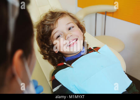 L'enfant aux cheveux bouclés se livre et grimaces dans un fauteuil dentaire Banque D'Images