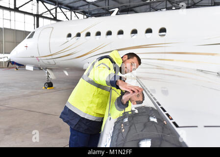 Mécanicien d'aéronefs inspecte et vérifie la technologie d'un jet dans un hangar à l'aéroport Banque D'Images