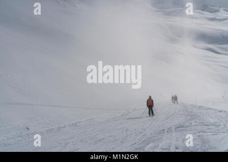 Les skieurs de disparaître dans la brume et les nuages bas sur une piste à Les Menuires dans le domaine skiable des Trois Vallées de la France pour une journée ensoleillée et lumineuse Banque D'Images