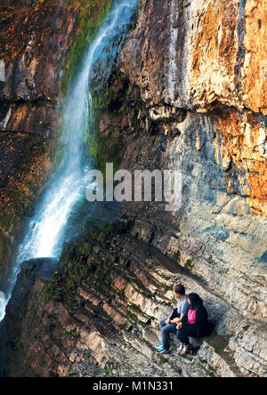 Youn couple rester sur le bord du rocher en haute montagne et wach belle cascade près de lui Banque D'Images