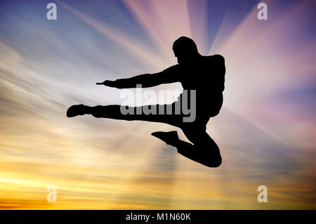 Silhouette de l'homme à coup de volant en fond de ciel coucher de soleil. Composition d'arts martiaux. Banque D'Images