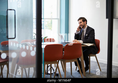 Jeune homme d'effectuer un appel téléphonique dans une salle de réunion Banque D'Images