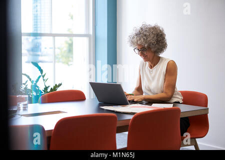 Smiling middle aged woman travaillant seul dans la salle de bureau Banque D'Images