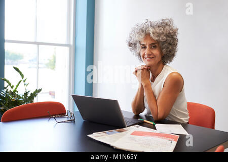 Femme d'âge moyen de travailler dans un bureau en souriant à l'appareil photo Banque D'Images