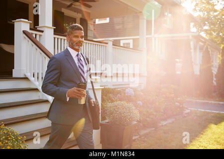 Businessman avec tasse de café laissant Suburban House pour travailler Banque D'Images