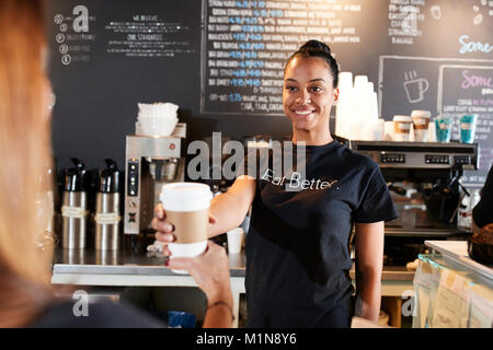 Barista femelle servant café à emporter avec client In Cafe Banque D'Images