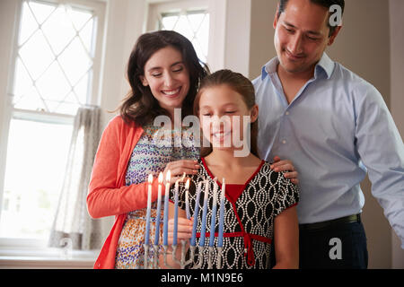 Fille de parents regarder la lumière des bougies sur la menorah pour Shabbat Banque D'Images