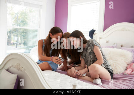 Teenage Girls sitting on bed together looking at smartphone Banque D'Images