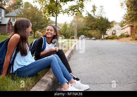 Deux copines adolescentes parle assis au bord de la route Banque D'Images