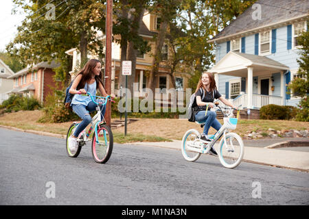 Deux copines adolescentes ride passé sur des vélos dans une rue calme Banque D'Images