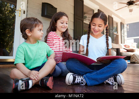 Groupe d'enfants s'asseoir sur le porche de la maison Lire des livres ensemble Banque D'Images