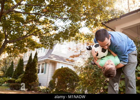 Père jouant avec un ballon de soccer dans jardin avec fils Banque D'Images