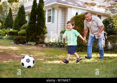 Grand-père joue au soccer dans jardin avec petit-fils Banque D'Images