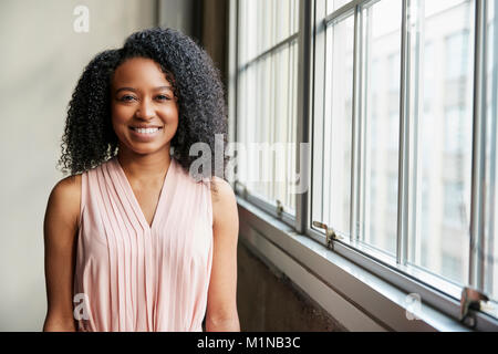 Jeune femme d'affaires noire par fenêtre à l'appareil photo Banque D'Images